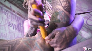 Septum lip rings and dread pompom pose on a wooden stand under purple neon
